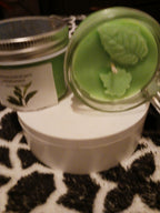 Green scented candle with leaf decorations in glass container on white round surface